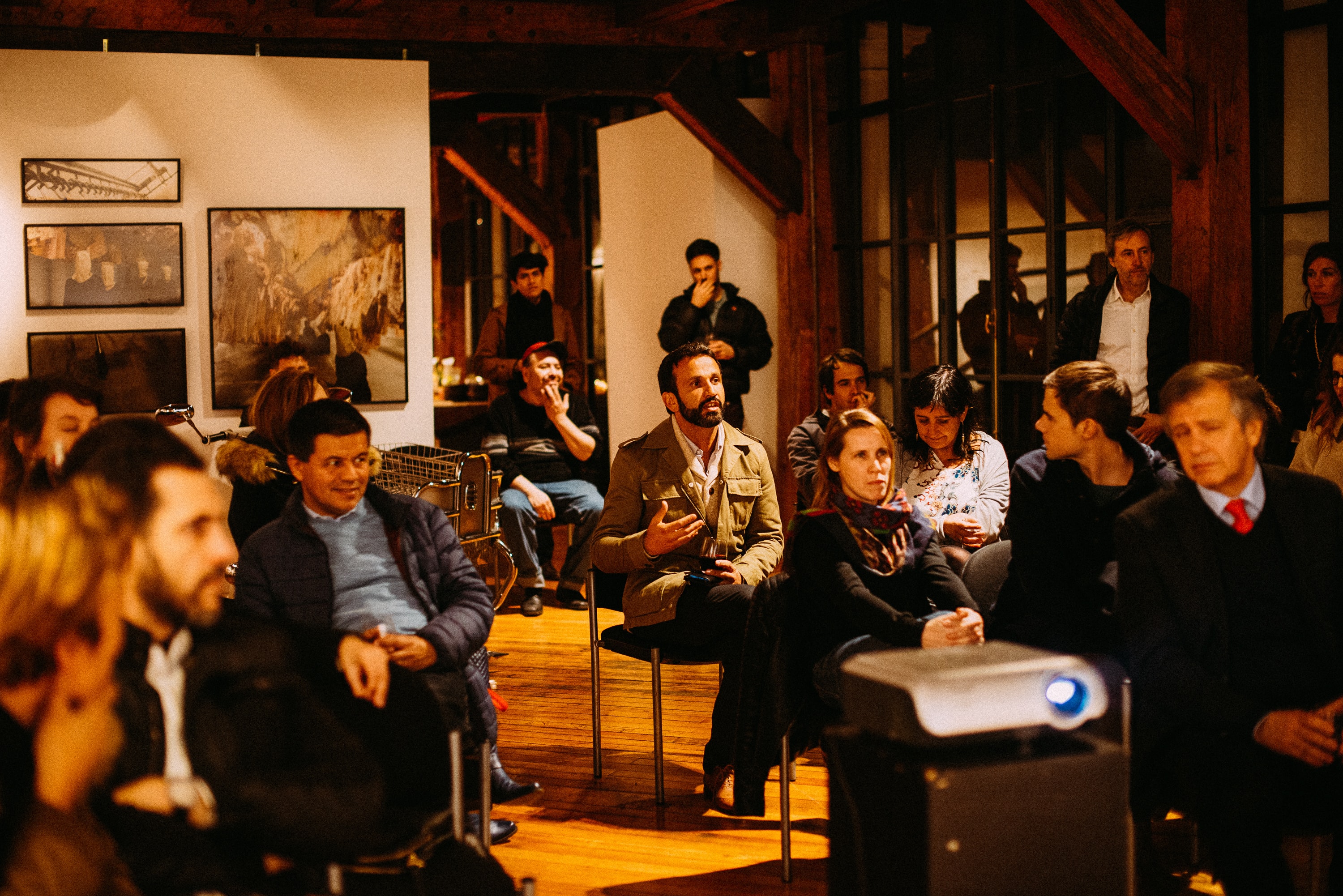 Photo of a well-groomed bearded man in focus, sitting in the center of a group attending a training session in an old wooden building with large wooden posts and beams, making a point to the speaker off-screen. Others onlooking/leaning in, with a large black and white photo artwork on a light beige rear wall in the background. The image represents the drive for continuous improvement in the Protopian philosophy, seeking knowledge and growth through learning from experienced Grandmasters. Click to learn more about the Protopian Grandmaster's Corner.