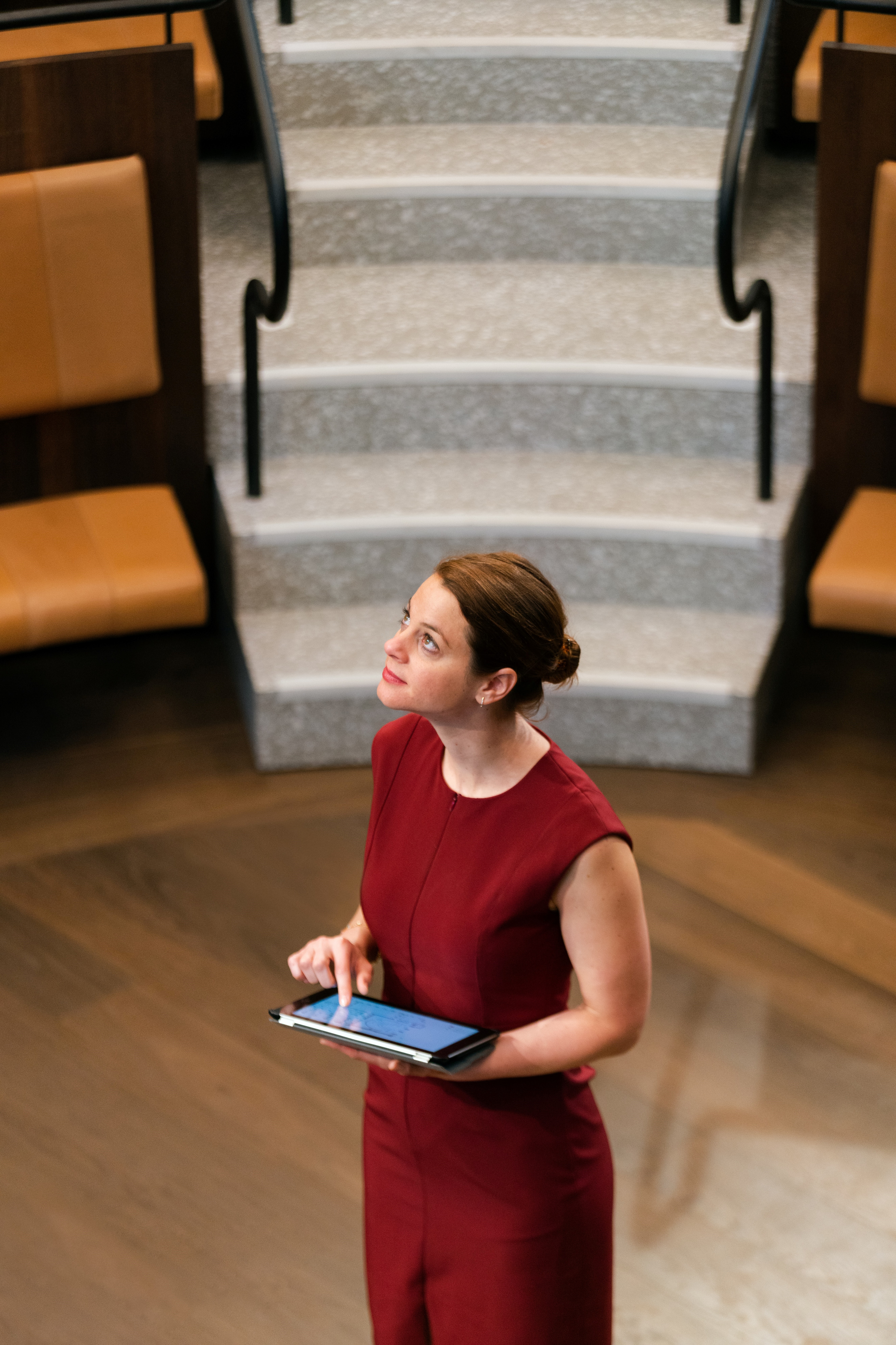 The section that states, “Business Protopia.”  The image is a young woman in a sleeveless red conservative red business type dress holding a computer tablet, and she is in the middle of what appears to be a small university lecture hall with steps rising 4 meters behind her head with medium brown hardwood flooring brown leather padded seats. She appears to be looking up at the words “Customer Protopia.” 